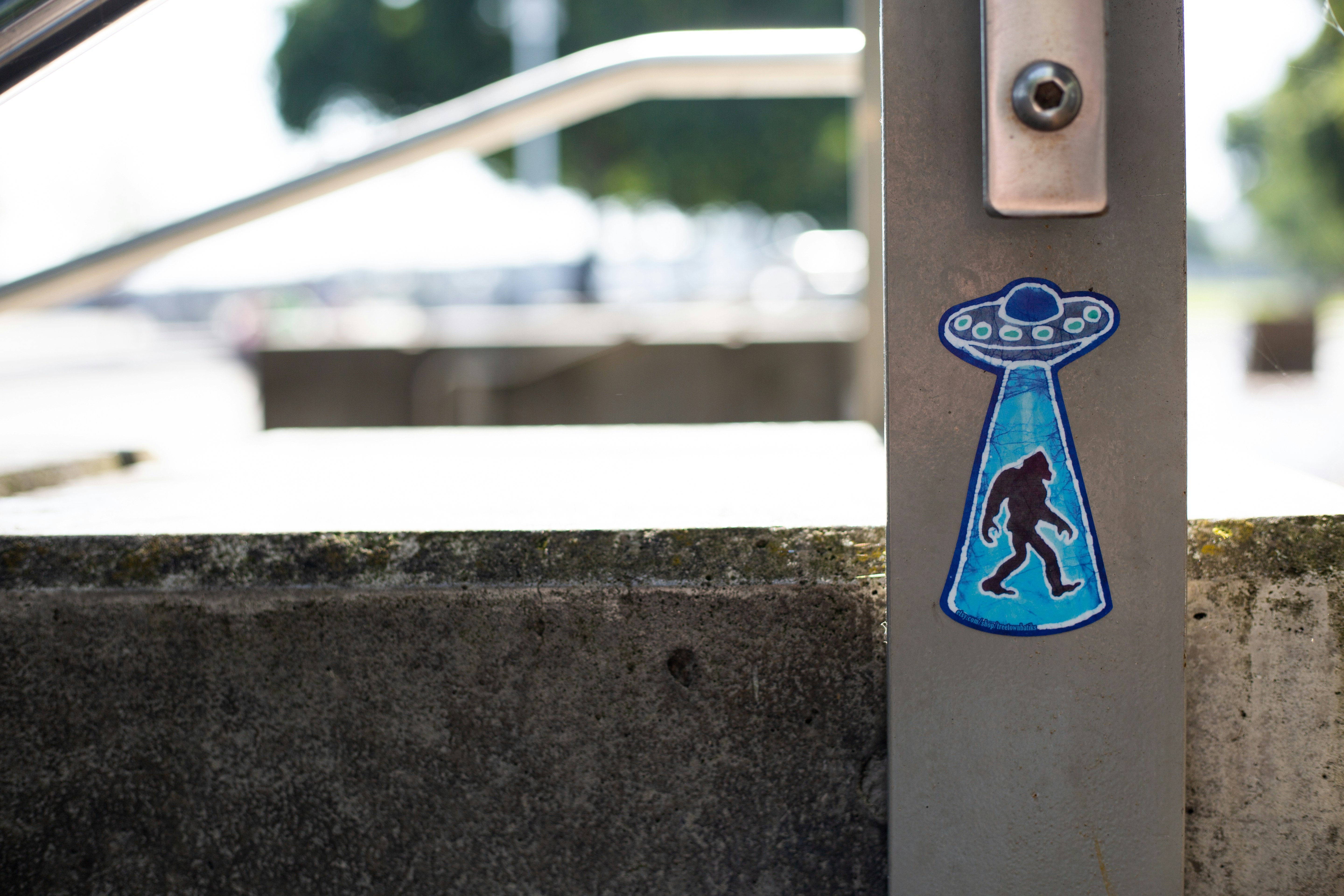 drawing of a blue UFO beaming up a black silhouette of bigfoot on a metal surface next to a wall