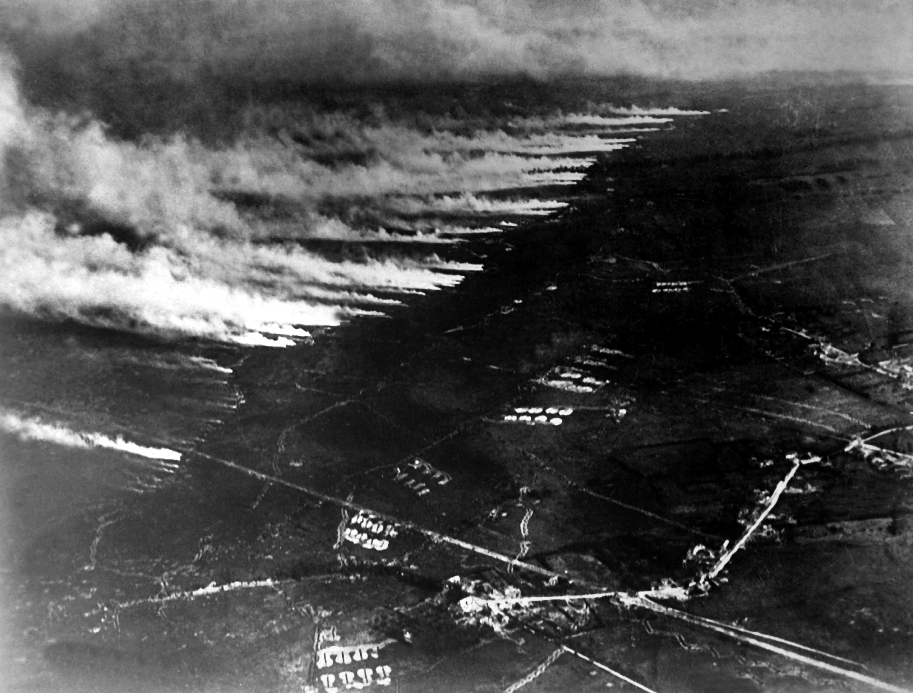 A black and white aerial photo showing a landscape covered in lines of gas clouds that are being released from the center of the image and flowing to the left. There are what appear to be roads and building visible in the darker space to the right-hand side of the image, but the quality is too dark to make out the details.