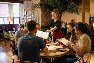 A group of friends looking at menus together in a restaurant, which have been given to them by a waitress.
